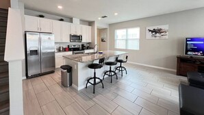 A modern kitchen with a central island, stainless steel appliances, and a bar area with stools. - #5135 Cozy Villa 4/4 Centrally Located Disney/Epic (Kissimmee)