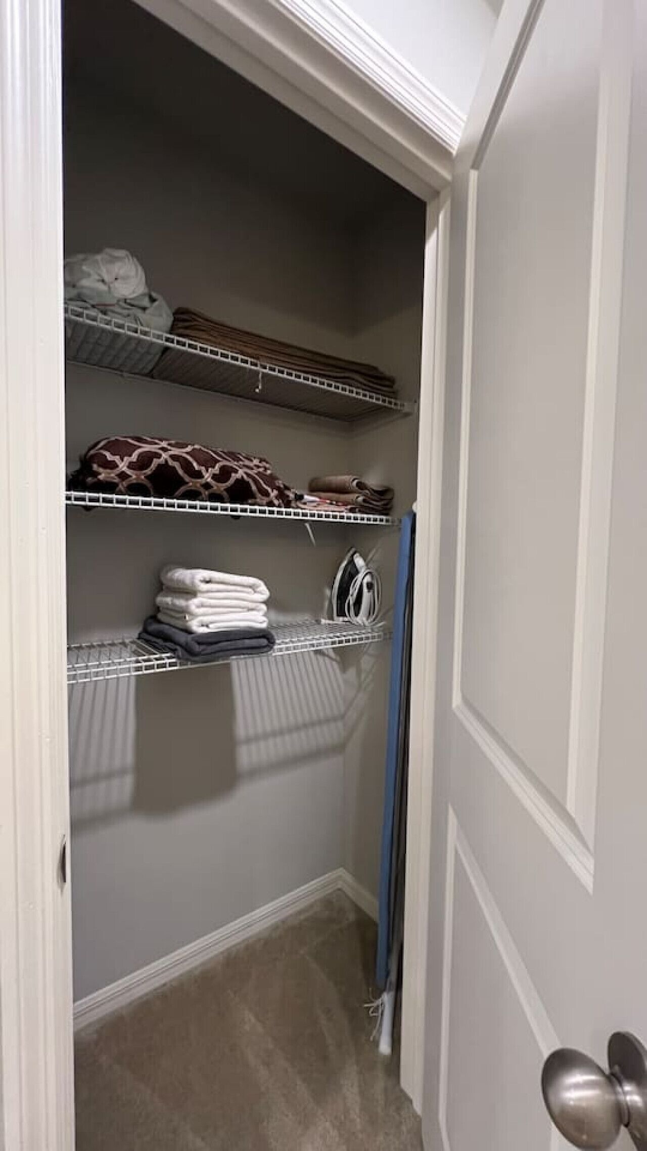 A closet with shelves containing folded towels, a rolled-up rug, and a hanging garment.