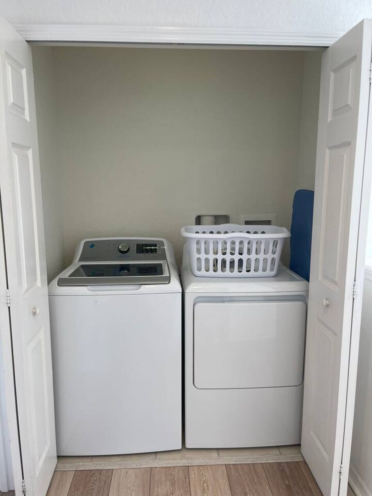 A laundry room with two stacked washers and dryers, a white laundry basket on the dryer, and a blue mat on the floor.