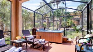 A glass-enclosed patio with a hot tub, wicker furniture, and a view of palm trees. - #2750 Cozy Resort 4/3.5 2 Masters Disney Universal (Kissimmee)