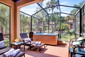 A glass-enclosed patio with a hot tub, wicker furniture, and a view of palm trees. - #2750 Cozy Resort 4/3.5 2 Masters Disney Universal (Kissimmee)