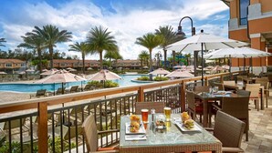 A poolside dining area with tables and chairs, overlooking a swimming pool and palm trees. - #2750 Cozy Resort 4/3.5 2 Masters Disney Universal (Kissimmee)