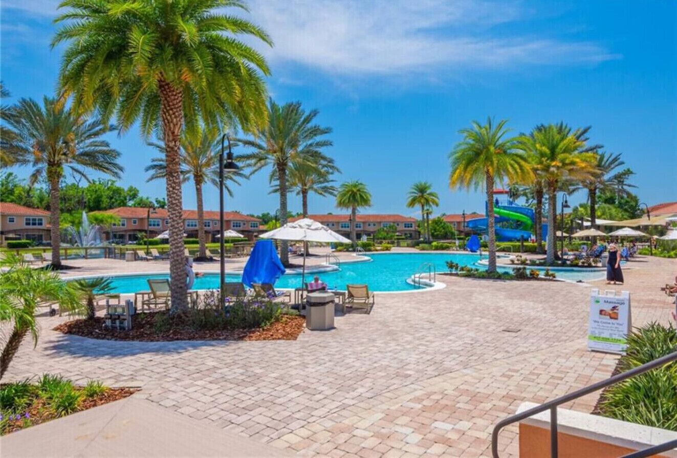 A resort pool area with palm trees, lounge chairs, and a water slide.