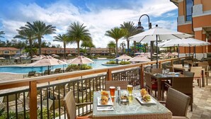 A poolside dining area with tables and chairs, a pool, and palm trees in the background. - #2731 Lakefront Priv Spa Pool Stunning Disney Epic (Kissimmee)