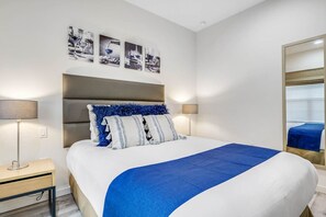 A modern hotel room with a large bed, two bedside lamps, a headboard with a fluffy pillow, and a series of black and white photographs on the wall. - 2647 Resort Suite • Spa & Pool • Near Disney+Uni (Kissimmee)