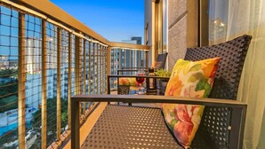A balcony with a view of high-rise buildings, a table with a glass, and a chair with a colorful cushion. - 1902 Luxury 2BD/2BA Lakefront• I-Drive+Universal (Orlando)