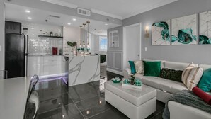 A modern living room with a white sofa, a coffee table, and a kitchen area with a refrigerator and cabinets. - 1902 Luxury 2BD/2BA Lakefront• I-Drive+Universal (Orlando)