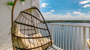 Una poltrona sospesa su un balcone con vista su un lago e edifici in lontananza.