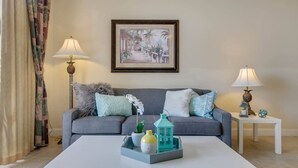 Un soggiorno con un divano grigio, due tavolini con lampade, un quadro incorniciato al muro e un tavolino da caffè con oggetti decorativi.