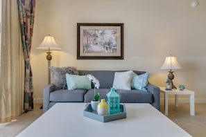Ein Wohnzimmer mit grauem Sofa, zwei Beistelltischen mit Lampen, einem gerahmten Bild an der Wand und einem Couchtisch mit Dekoration.