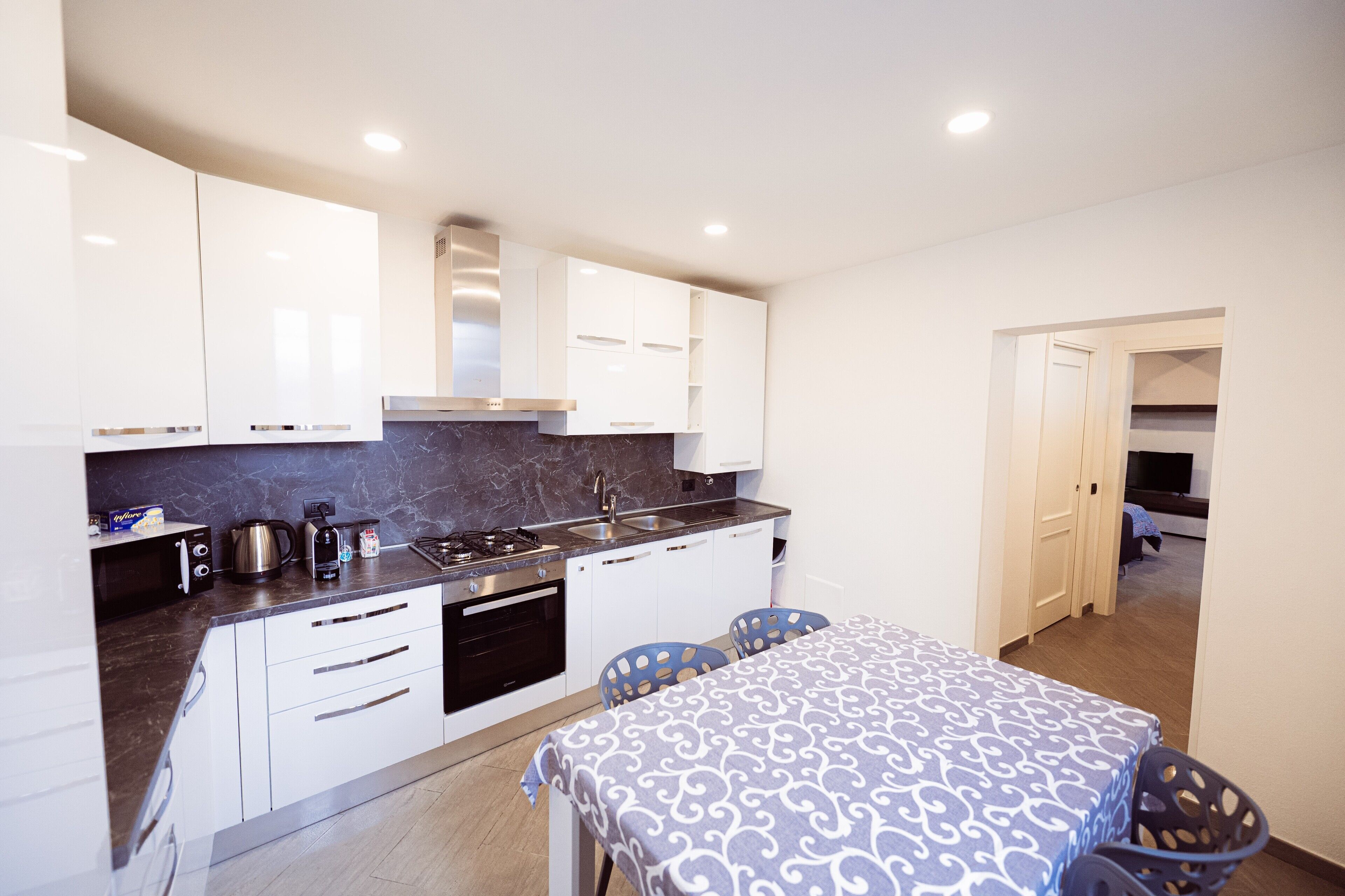 A modern kitchen with white cabinets, a marble countertop, and a dining area with a patterned tablecloth.