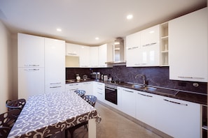 Una cocina moderna con armarios blancos, encimera de mármol y zona de comedor con mantel estampado.