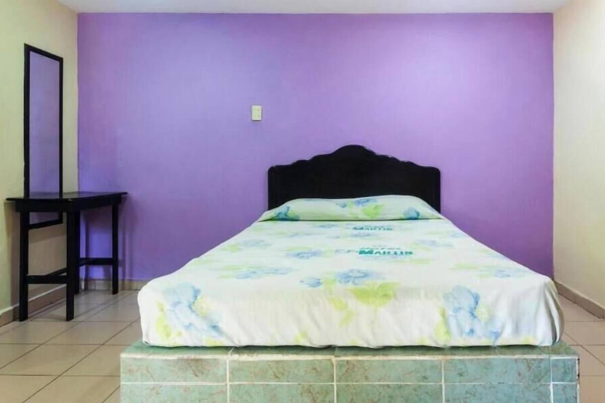 Una cama individual con una colcha estampada con motivos florales, un cabecero negro y una mesita de noche a la izquierda.