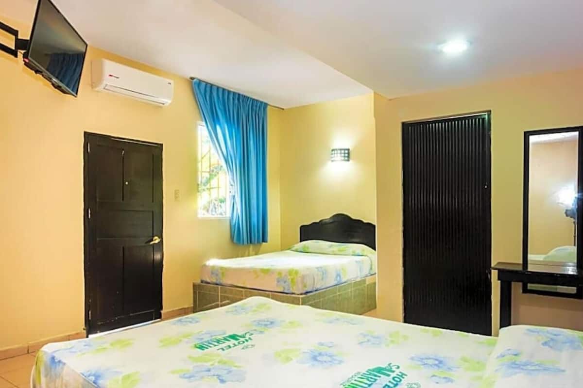 Habitación de hotel con dos camas, un televisor, aire acondicionado, una ventana con cortinas azules y un espejo.