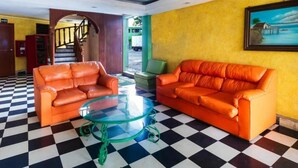 Un hall d’entrée avec un sol à carreaux, deux canapés en cuir orange, une table basse en verre et un escalier en arrière-plan.