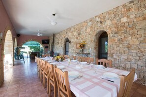 A dining area with a stone wall, a checkered tablecloth, and wooden chairs. - Villa 'I Sogni Di Venere' with Sea View, Wi-Fi and Air Conditioning (Torre Suda)