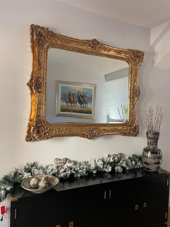 A mirror with an ornate gold frame, a painting, and a decorative arrangement on a black cabinet. - Luxury cottage with hot tub. Sleeps up to 6. Pet-Friendly. (Kilham)