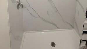 A shower with a white marble wall, a showerhead, a towel rack, and a shower control panel. - STARLITE MOTEL (Fraser)