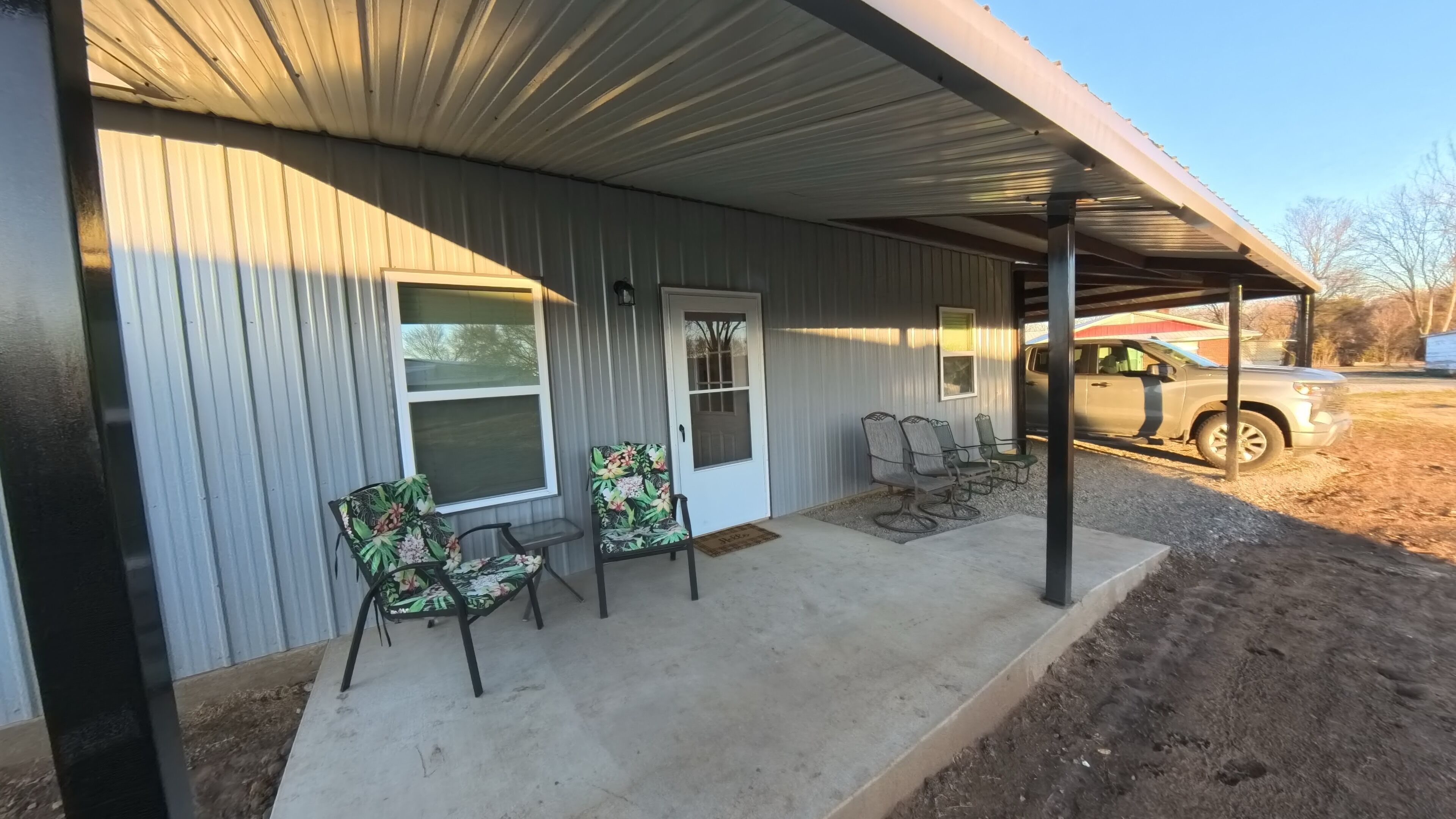 A covered porch with two chairs and a door, a parked truck, and a clear sky.