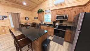 Eine Holz-Blockhausküche mit Granit-Arbeitsplatten, einem Edelstahl-Kühlschrank, einer Mikrowelle, einem Backofen und einem Spülbecken.