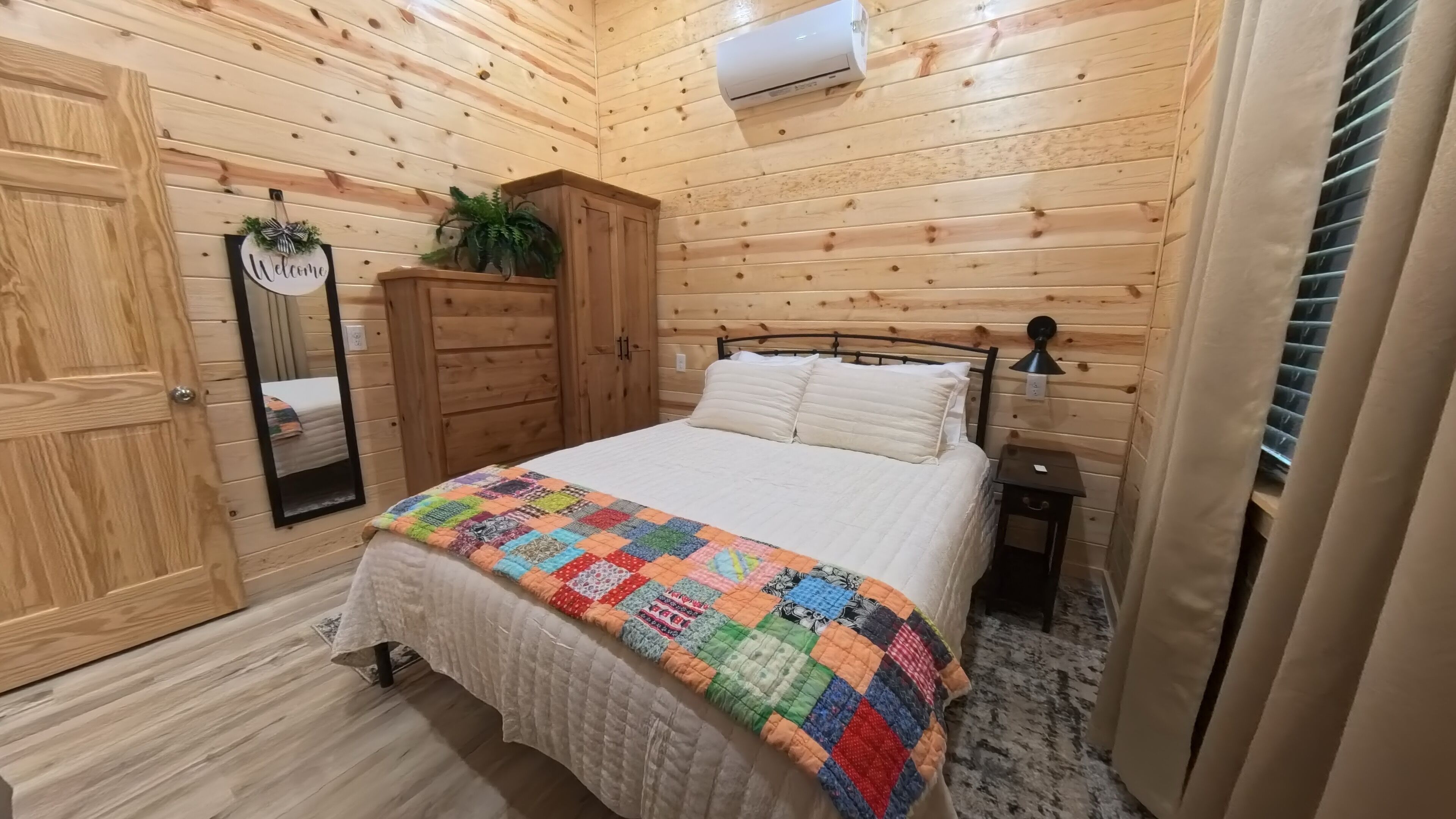 A wooden-paneled bedroom with a bed, a nightstand, a mirror, and a wardrobe.