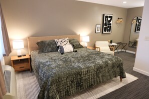 A neatly arranged bedroom with a large bed, two bedside tables with lamps, a chair, a small table, and a mirror. - Jackrabbit 132| Modern Downtown Moab| Arches (Moab)