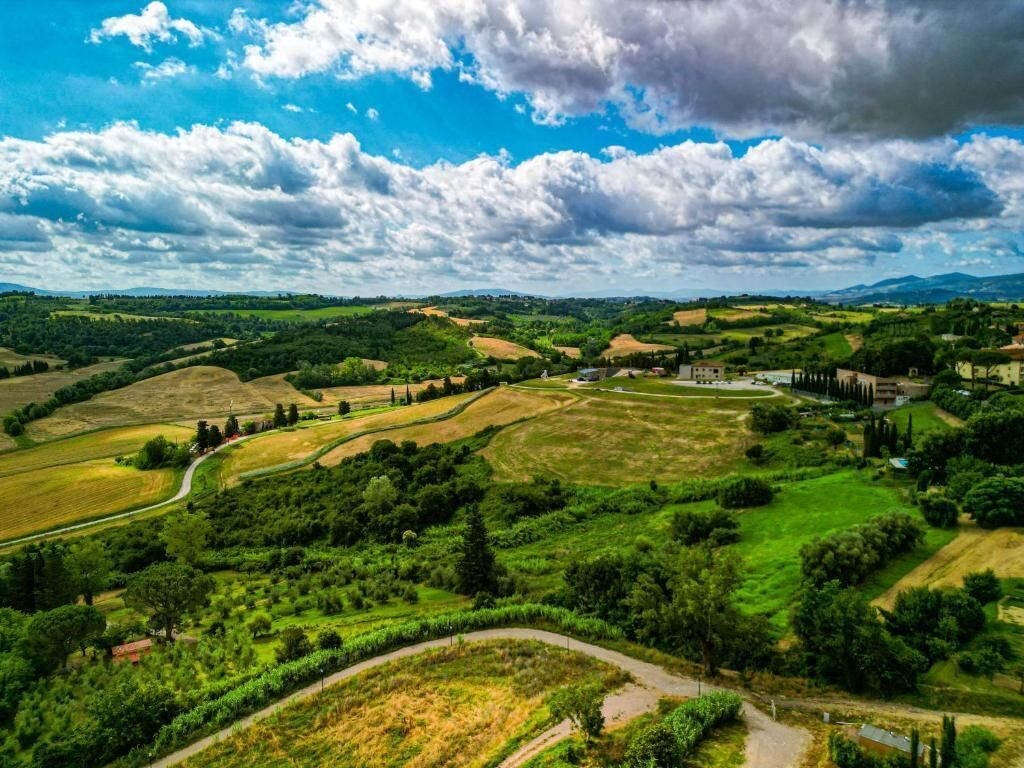 Vista panorâmica de uma paisagem rural com colinas onduladas, uma estrada sinuosa e edifícios dispersos.