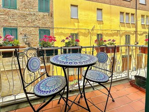 Een ronde tafel met blauw gestreepte stoelen op een balkon met terracotta tegels.