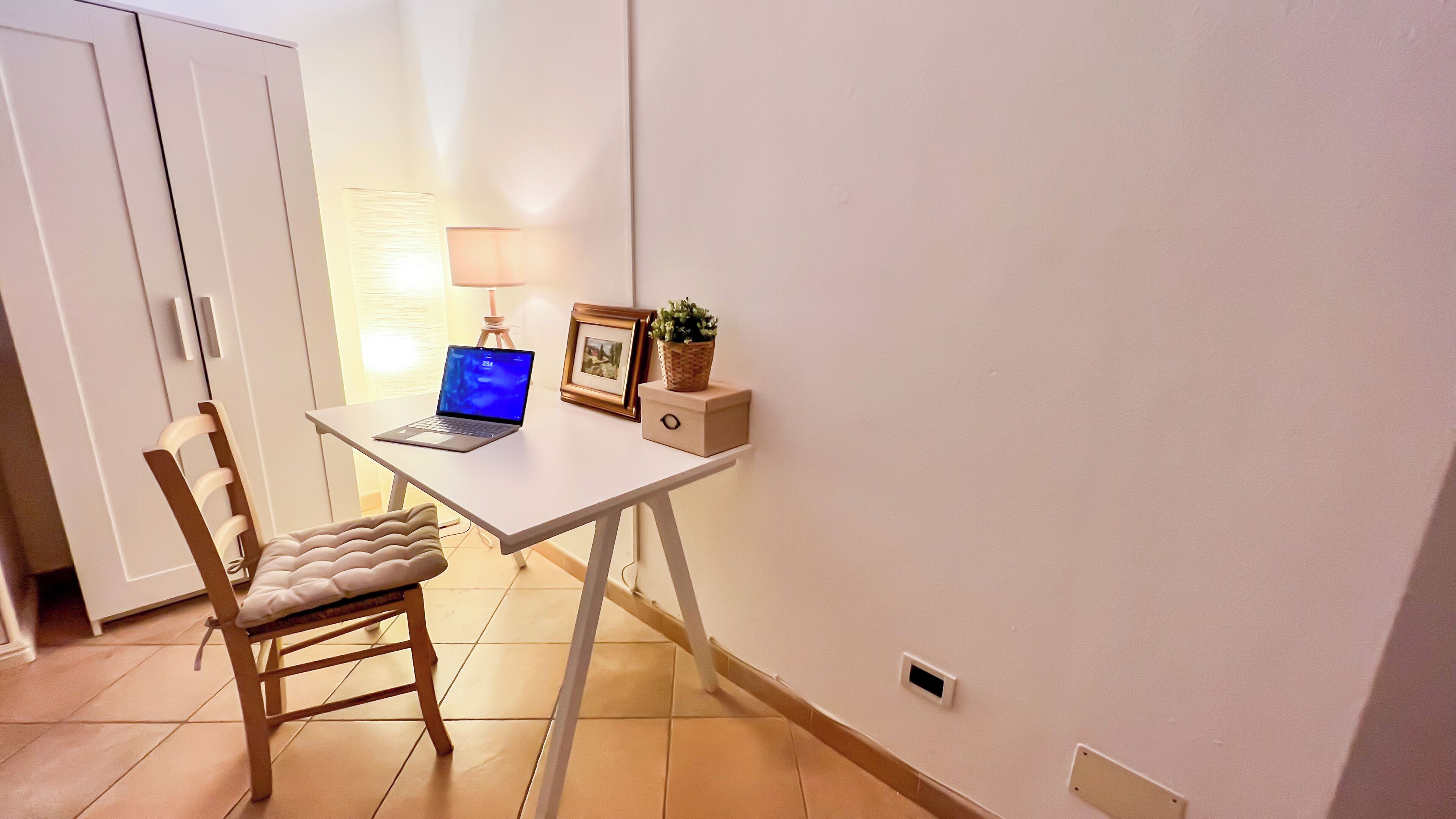 Una habitación pequeña y ordenada con escritorio, silla y una computadora portátil.