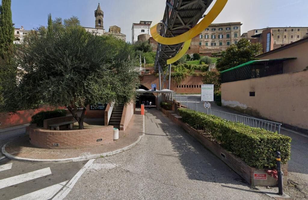 Uma área de estacionamento com uma árvore, entrada de prédio e escadas.