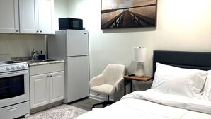 Habitación de hotel con cama, escritorio, silla, kitchenette y un cuadro en la pared.