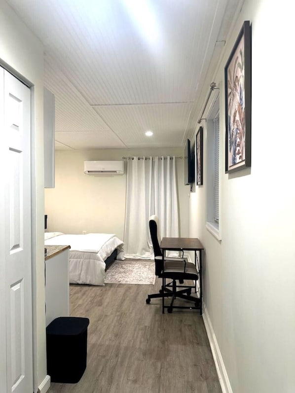 A compact room with a bed, a desk, a chair, an air conditioner, and a window with curtains.