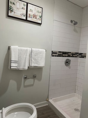 A bathroom with a toilet, a shower, and a towel rack with two towels.