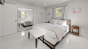 Une chambre moderne avec un grand lit, un banc, une table de chevet et un miroir.