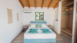 Un dormitorio con una cama, un armario de madera, una ventana con marco verde y un tapiz de macramé en la pared.