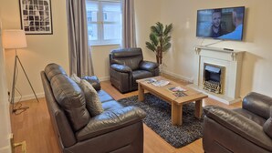 A living room with a sofa, armchair, and a coffee table. There is a fireplace, a television, and a plant. - Spacious Modern 2-BR Apartment in Aberdeen City Centre (Aberdeen)