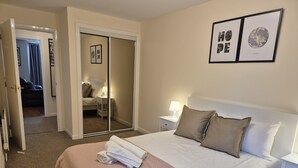 A hotel room with a bed, a nightstand, a mirror, and a door leading to another room. - Spacious Modern 2-BR Apartment in Aberdeen City Centre (Aberdeen)