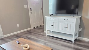 A room with a wooden table, a white cabinet with a television, and a door. - Spacious NEW townhome w/Fast WiFi and parking (Glendale)