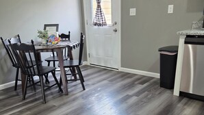 A dining area with a wooden table and chairs, a kitchen area with a dishwasher, and a door with a checkered curtain. - Spacious NEW townhome w/Fast WiFi and parking (Glendale)