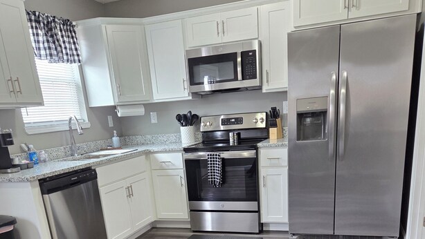 A modern kitchen with white cabinets, stainless steel appliances, and a grey wood floor. - Spacious NEW townhome w/Fast WiFi and parking (Glendale)