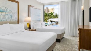 Habitación de hotel con dos camas, una lámpara, un televisor y vistas a una piscina y edificios.