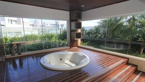 Ein modernes Badezimmer mit Holzboden, einer großen Badewanne und großen Fenstern mit Blick auf Grünflächen und Gebäude.