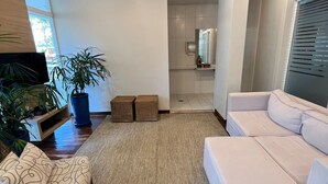Ein modernes Wohnzimmer mit Holzboden, einem großen Fenster, einer Couch, einem Sessel und einem Blumentopf.