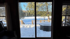 Una stanza con un'ampia porta-finestra che si apre su una zona esterna innevata, con un pontile in legno e una vasca idromassaggio.