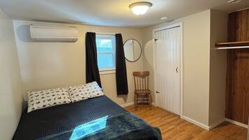 A bedroom with a bed, a chair, a wardrobe, a window, and an air conditioning unit.