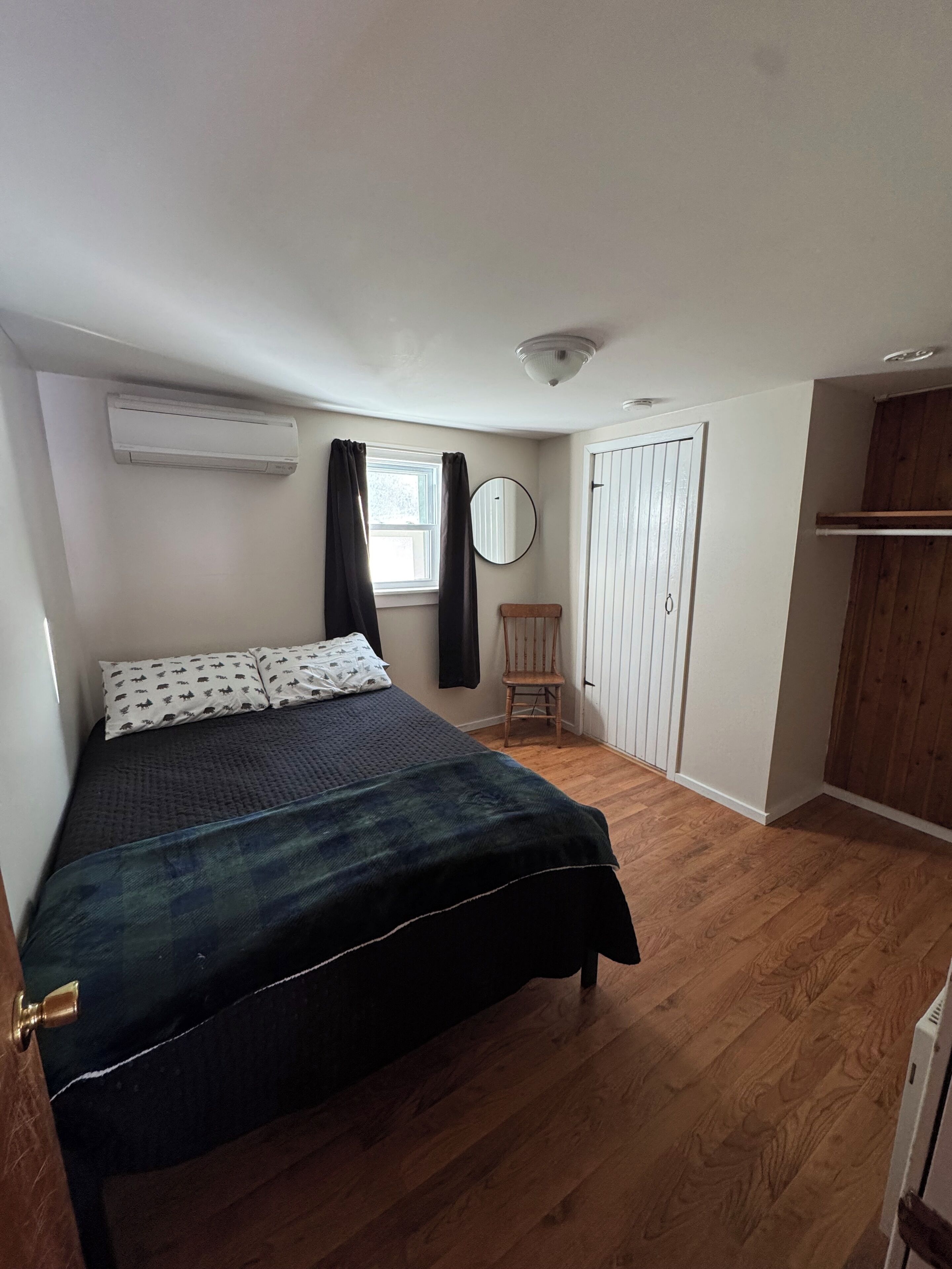 A bedroom with a bed, a chair, a wardrobe, and an air conditioning unit.