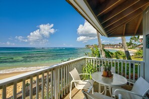 Un balcon doté d’une balustrade blanche, d’une table ronde et de deux chaises blanches, offrant une vue sur une plage et l’océan.