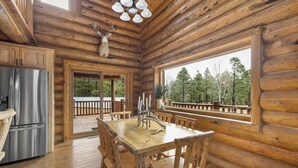 Interior rústico de una cabaña con una mesa de comedor de madera, sillas, un refrigerador y una cabeza de venado montada en el techo.