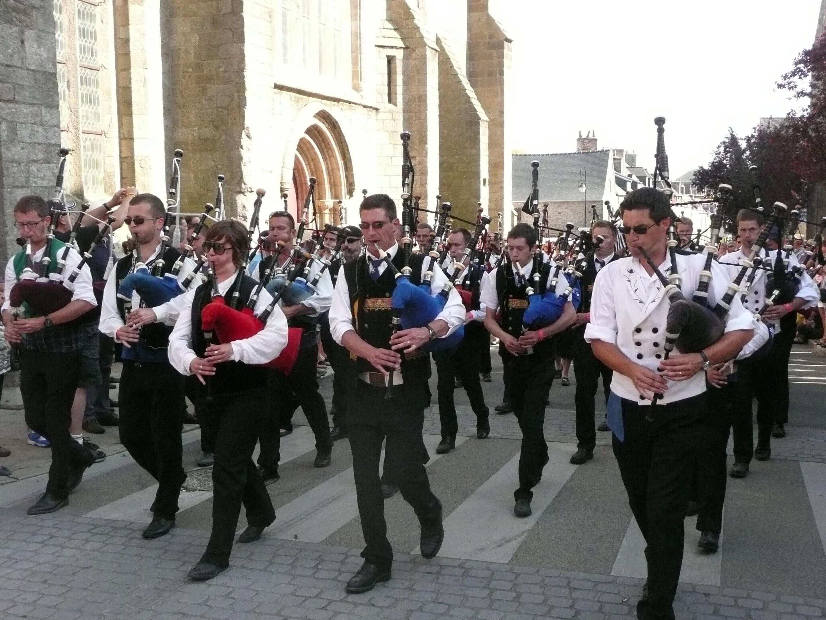 A group of men in traditional attire playing bagpipes in a public square.