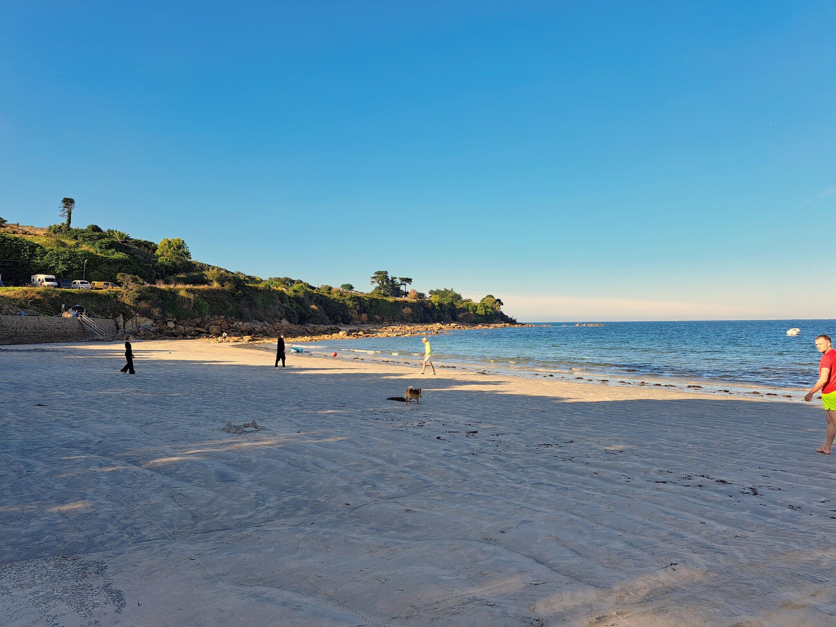 A beach with a clear sky, calm sea, and a few people walking.